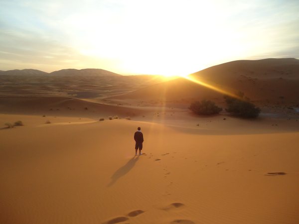 photo of a man standing alone in the sandy desert at dusk